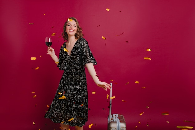 Foto de estudio de alegre mujer caucásica en vestido largo vintage tatsing vino