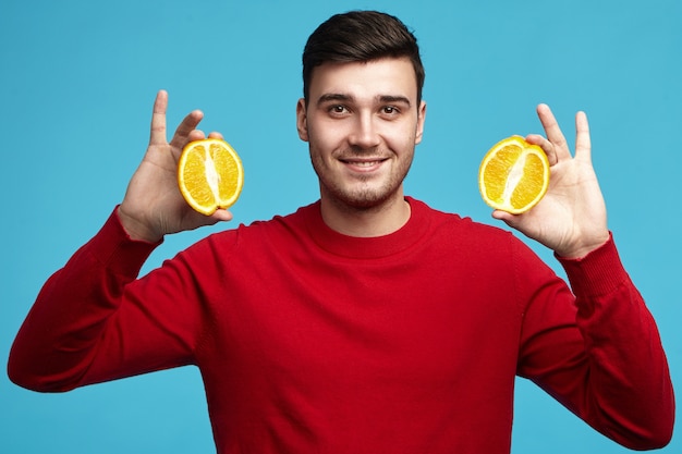 Foto gratuita foto de estudio de apuesto joven vegetariano masculino europeo positivo en suéter rojo posando en la pared azul