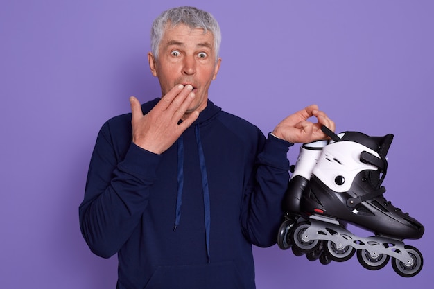 Foto de estudio de asombroso hombre senior de pelo blanco con patines en manos