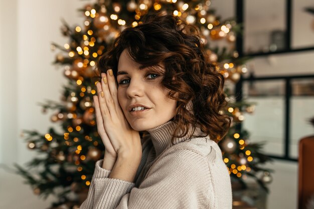 Foto de estudio de atractiva mujer de cabello oscuro con cabello ondulado posando de árbol de Navidad, Año Nuevo, Navidad