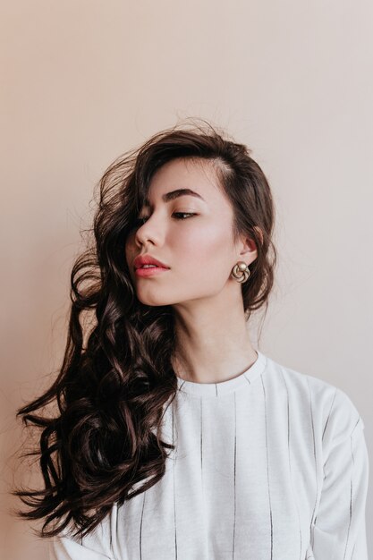 Foto de estudio de atractiva mujer China mirando a otro lado. Sensual mujer asiática posando en aretes de oro.