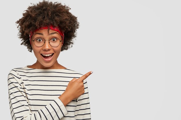 Foto de estudio de chica de piel oscura positiva lleva gafas transparentes redondas