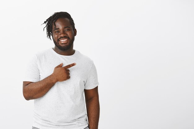 Foto de estudio de chico feliz con trenzas posando contra la pared blanca