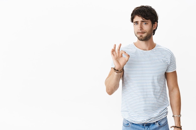 Foto gratuita foto de estudio de un compañero de trabajo europeo joven inseguro presionado y cansado que muestra un gesto correcto mientras frunce los labios sintiéndose preocupado e incómodo para estar de acuerdo en algo desagradable y molesto. copia espacio