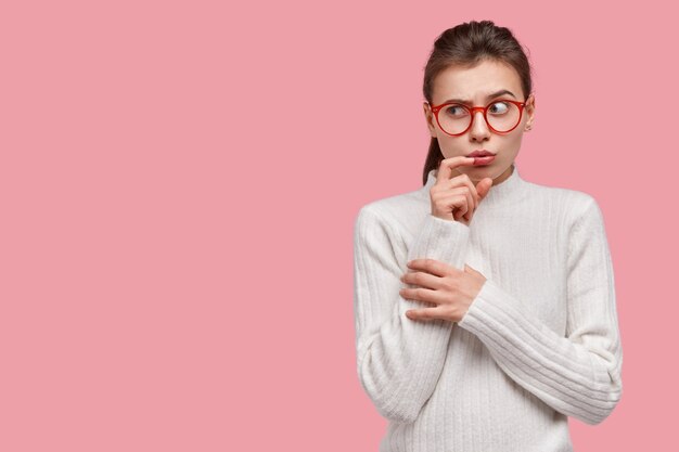 Foto de estudio de desconcertado mujer caucásica mantiene la mano cerca de la boca, se ve confusamente a un lado, vestida con ropa interior, grandes espectáculos