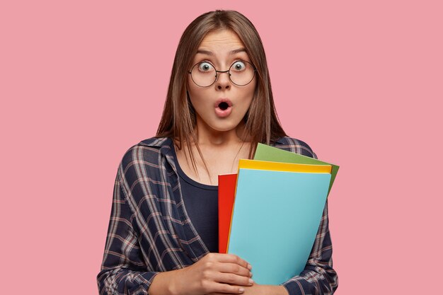 Foto de estudio de emocional joven mujer caucásica con ojos saltones, abre la boca del asombro