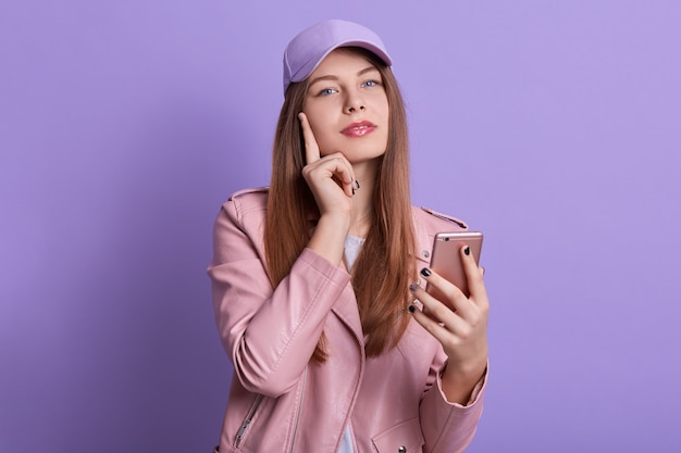 Foto de estudio de encantadora dama mirando directamente a la cámara mientras sostiene el teléfono inteligente en las manos