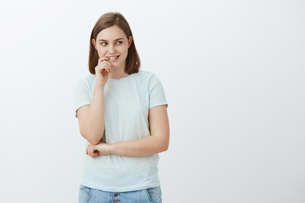 Foto de estudio de una estudiante atractiva inteligente y creativa con lindas orejas aleteadas mordiéndose el dedo mientras es curiosa e interesada smuling misteriosamente mirando a la derecha con deseo y emoción