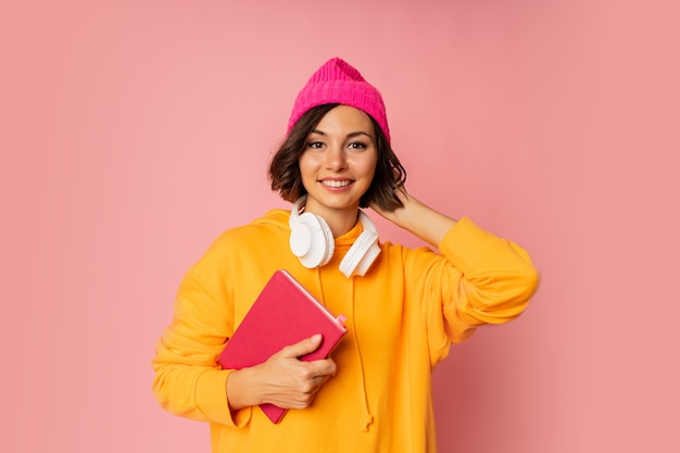 Foto de estudio de estudiante lindo feliz con cuadernos y auriculares en rosa.