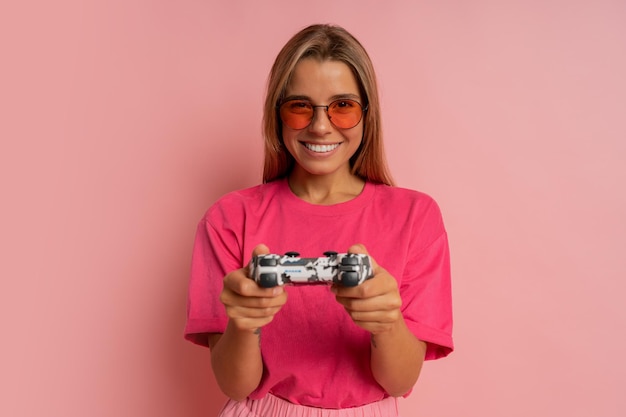 Foto de estudio de una feliz y emocionada mujer sonriente loca jugando videojuegos adicta a la playstation aislada en un fondo de color rosa