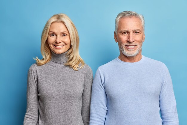 Foto de estudio de feliz mujer madura y hombre expresa emociones positivas disfrutar de la vida esperar a que los niños vengan vestidos con poloneck casual aislado sobre la pared azul del estudio