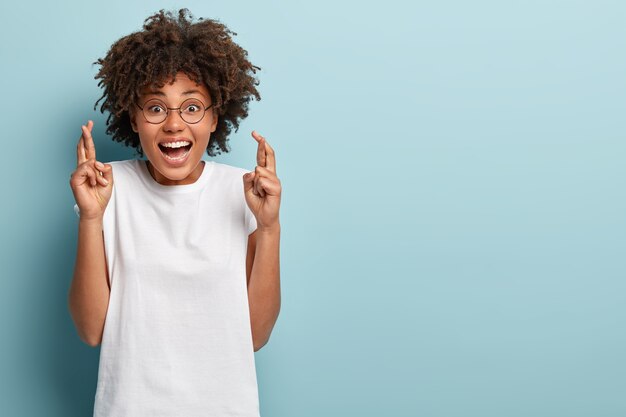 Foto de estudio de feliz mujer de piel oscura cruza los dedos para la buena suerte