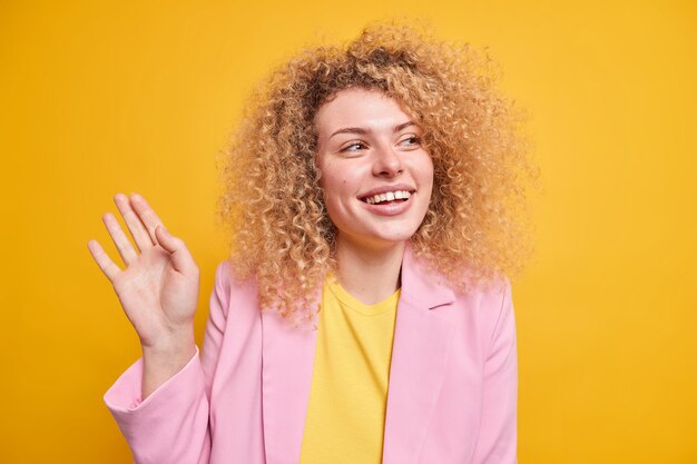 Foto de estudio de feliz sincera mujer europea con cabello rizado y tupido