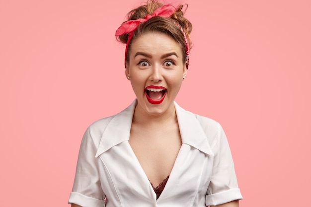 Foto de estudio de hermosa mujer alegre que mira sorprendentemente a la cámara, abre los ojos y la boca ampliamente, se siente asombrado al recibir un regalo inesperado