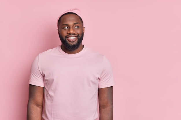 Foto de estudio de hombre afroamericano de piel oscura con barba espesa mira con alegría a un lado de estar de buen humor