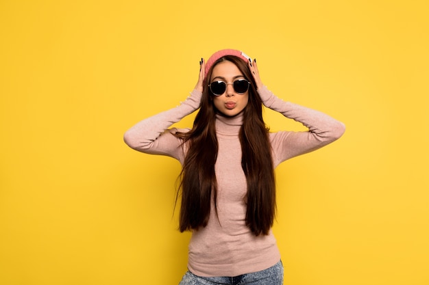 Foto de estudio en interiores de moda mujer elegante con cabello largo oscuro con gorra rosa y gafas negras Vista frontal de la mujer feliz