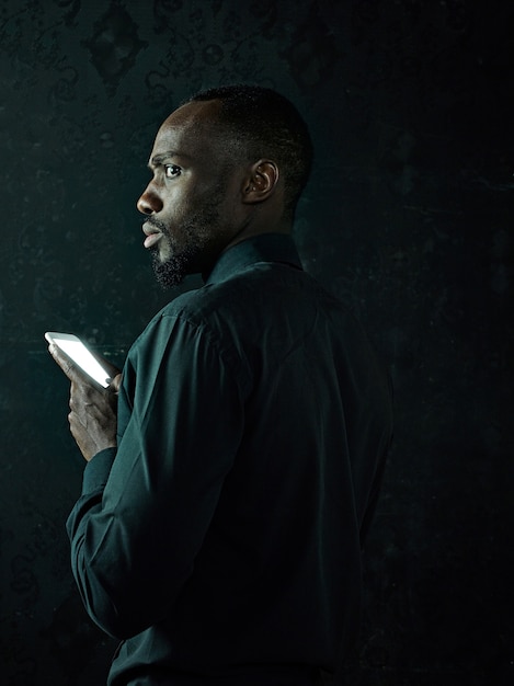 Foto de estudio de un joven africano negro serio pensando mientras habla por teléfono móvil contra el fondo negro del estudio