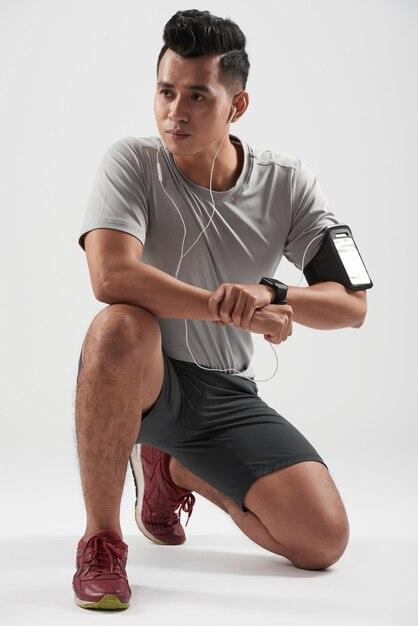 Foto de estudio del joven deportista asiático arrodillado y posando con sus dispositivos