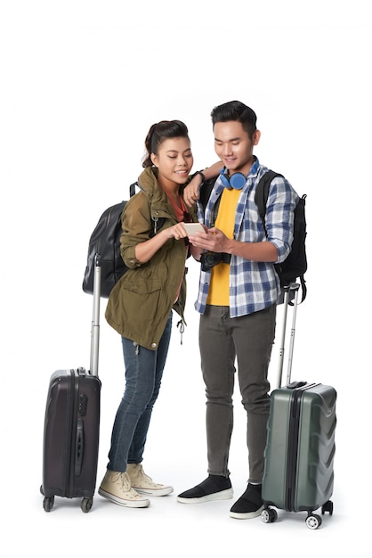 Foto de estudio de una joven pareja con equipaje navegando por la red en el teléfono inteligente
