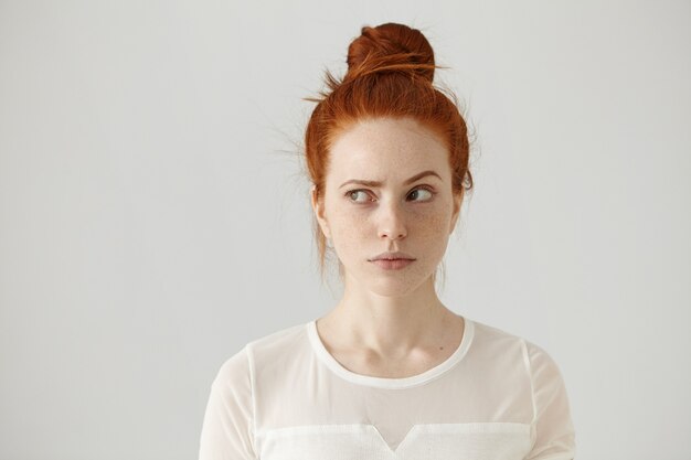 Foto de estudio de linda chica pelirroja con nudo de pelo y pecas mirando hacia los lados