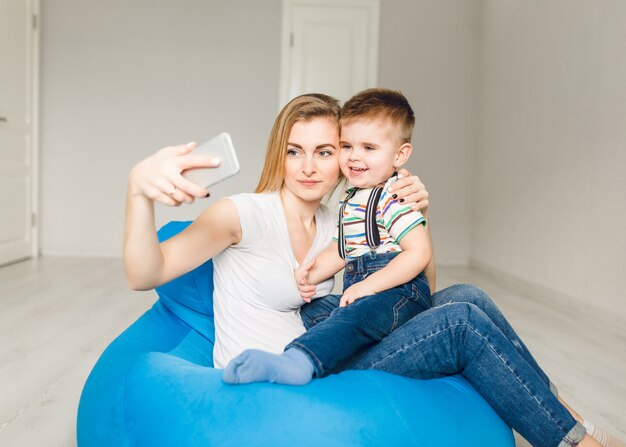 Foto de estudio de una madre sosteniendo a su hijo y tomando un selfie en smartphone