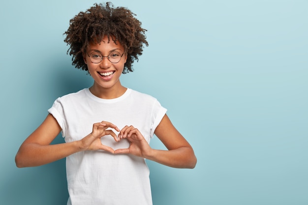 Foto de estudio de modelo femenino encantada envía gesto de corazón, confiesa enamorado, mira a la cámara felizmente