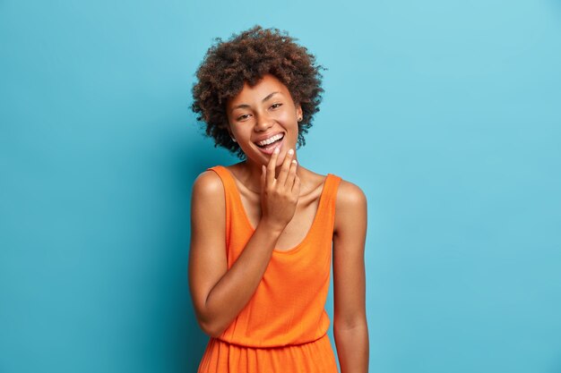 Foto de estudio de mujer afroamericana alegre despreocupada mira a la cámara felizmente