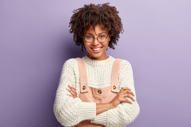 Foto de estudio de mujer agradable de aspecto agradable con peinado afro, disfruta de la vida, sonríe suavemente