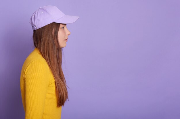 Foto de estudio de la mujer con gorra de béisbol y camisa amarilla, vista lateral de la atractiva mujer mirando hacia adelante