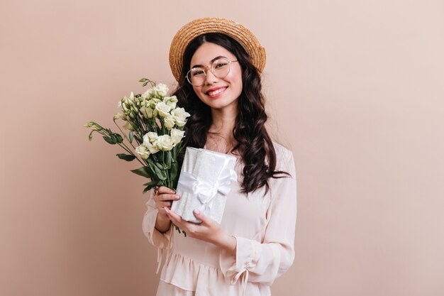 Foto de estudio de mujer japonesa con flores blancas. Encantadora modelo asiática con ramo de eustoma y regalo.