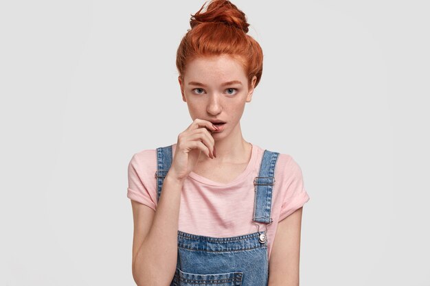 Foto de estudio de mujer jengibre pecoso con expresión seria y perpleja