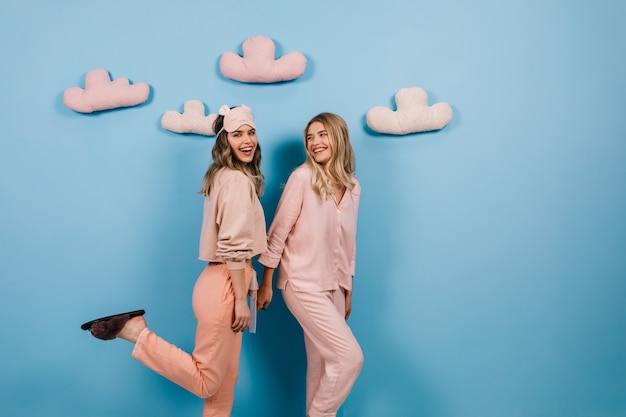 Foto de estudio de mujeres en pijama de pie sobre la pared azul con nubes de juguete