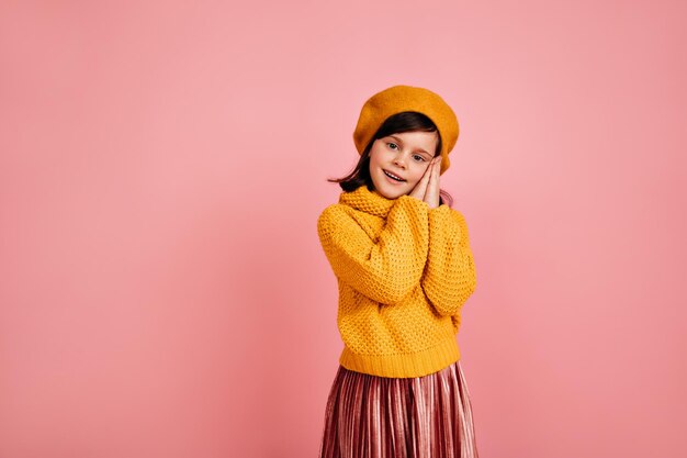 Una foto de estudio de una niña bonita con suéter de punto Niña extasiada de pie sobre fondo rosa