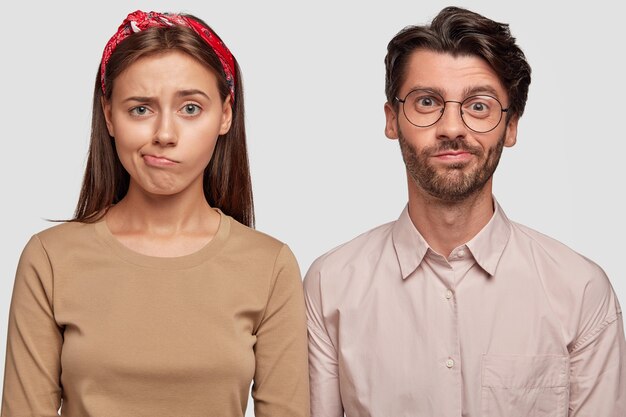 Foto de estudio de pareja joven confundida posando contra la pared blanca