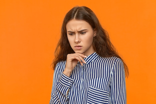 Foto de estudio de pensativa joven mujer de cabello oscuro vistiendo elegante camisa a rayas mano