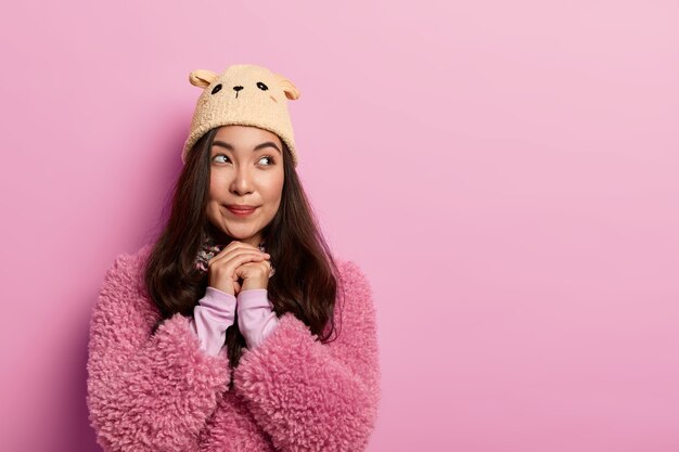 Foto de estudio de soñadora modelo femenino milenario contemplativo se encuentra con las palmas juntas cerca de la cara, mira a un lado, el deseo de los sueños se hace realidad