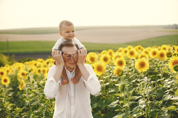 Foto de una familia joven en el campo de girasoles en un día soleado. Padre morena y su pequeño hijo rubio posando para una foto