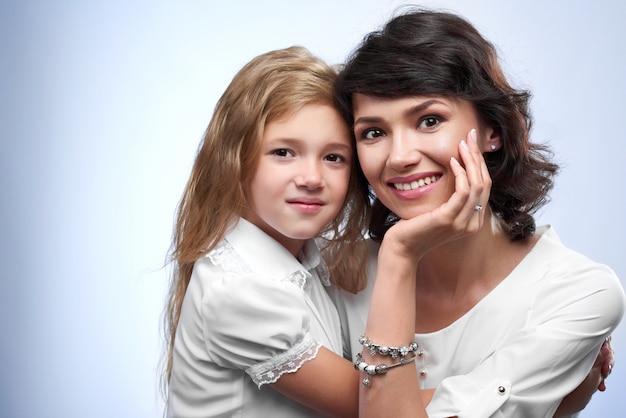 Foto de familia de una pareja feliz: sonriendo a una madre y su amada hija. Son muy bonitas y simpáticas. Eran camisetas blancas y se abrazan.