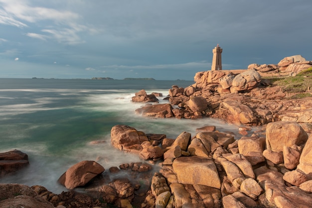 Foto de un faro de pie a la orilla del mar bajo el cielo nublado