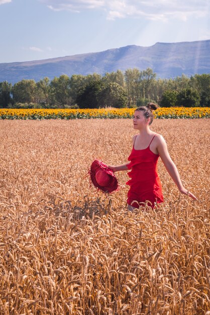 Foto fascinante de una mujer atractiva en un vestido rojo posando al frente en un campo de trigo