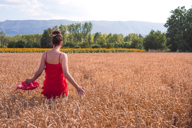 Foto fascinante de una mujer atractiva en un vestido rojo posando en un campo de trigo