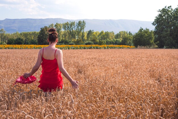 Foto fascinante de una mujer atractiva en un vestido rojo posando en un campo de trigo