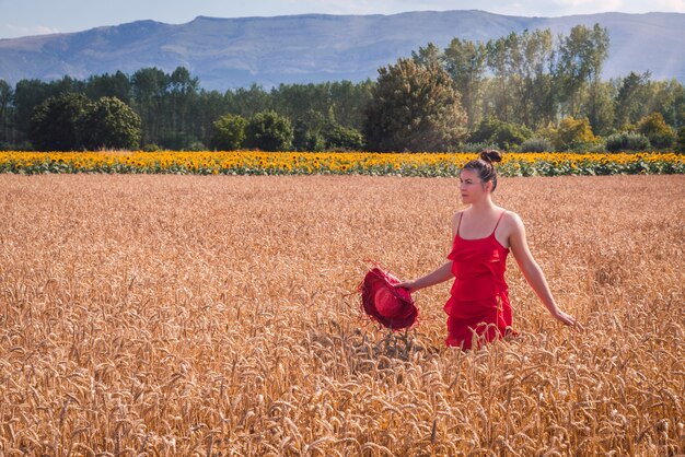 Foto fascinante de una mujer atractiva en un vestido rojo posando en un campo de trigo