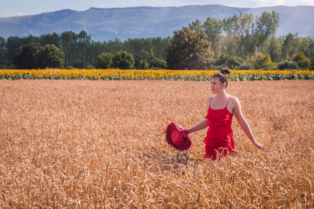 Foto fascinante de una mujer atractiva en un vestido rojo posando en un campo de trigo