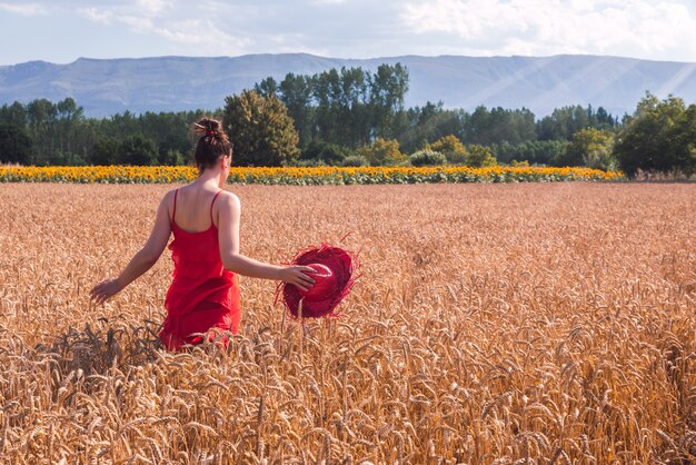 Foto fascinante de una mujer atractiva en un vestido rojo posando en un campo de trigo