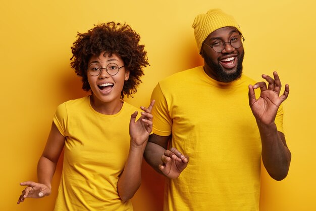 Foto de la feliz pareja africana bailan juntos contra el fondo amarillo, mueven el cuerpo activamente