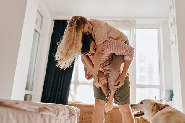 Una foto de una feliz pareja joven animando y mirando a su perro El hombre de cabello oscuro lleva a su dulce novia en la espalda