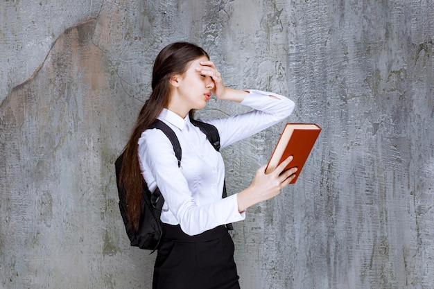 Una foto de una hermosa adolescente con mochila mirando un libro. foto de alta calidad