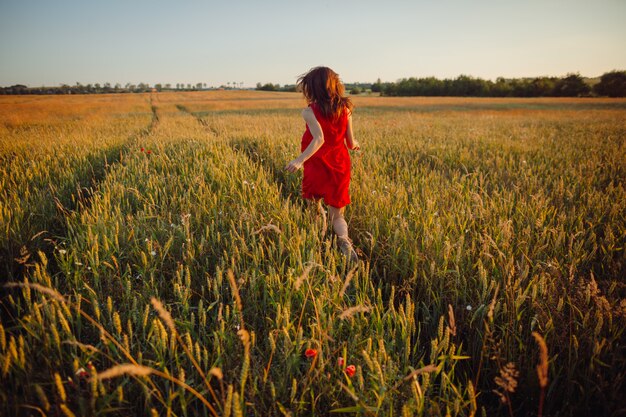 Foto de la hermosa dama en vestido rojo de pie en el campo de oro del verano
