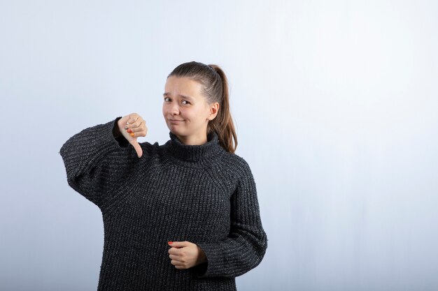 Foto de hermosa joven dando pulgares hacia abajo en gris.